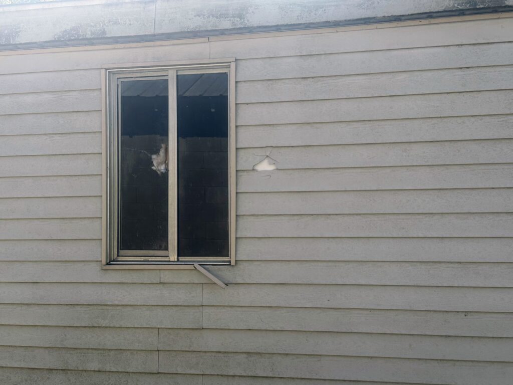 Close-up of a damaged window on a home's siding in Owen County, Indiana, after a hailstorm, requiring repair services.