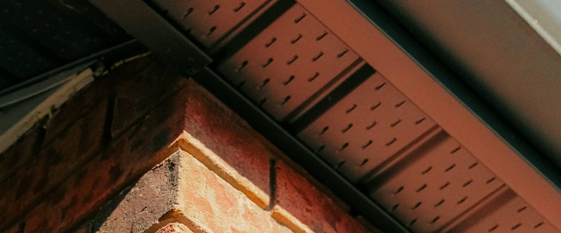 Close-up view of a house soffit and fascia, highlighting the perforated soffit panels and brick wall.