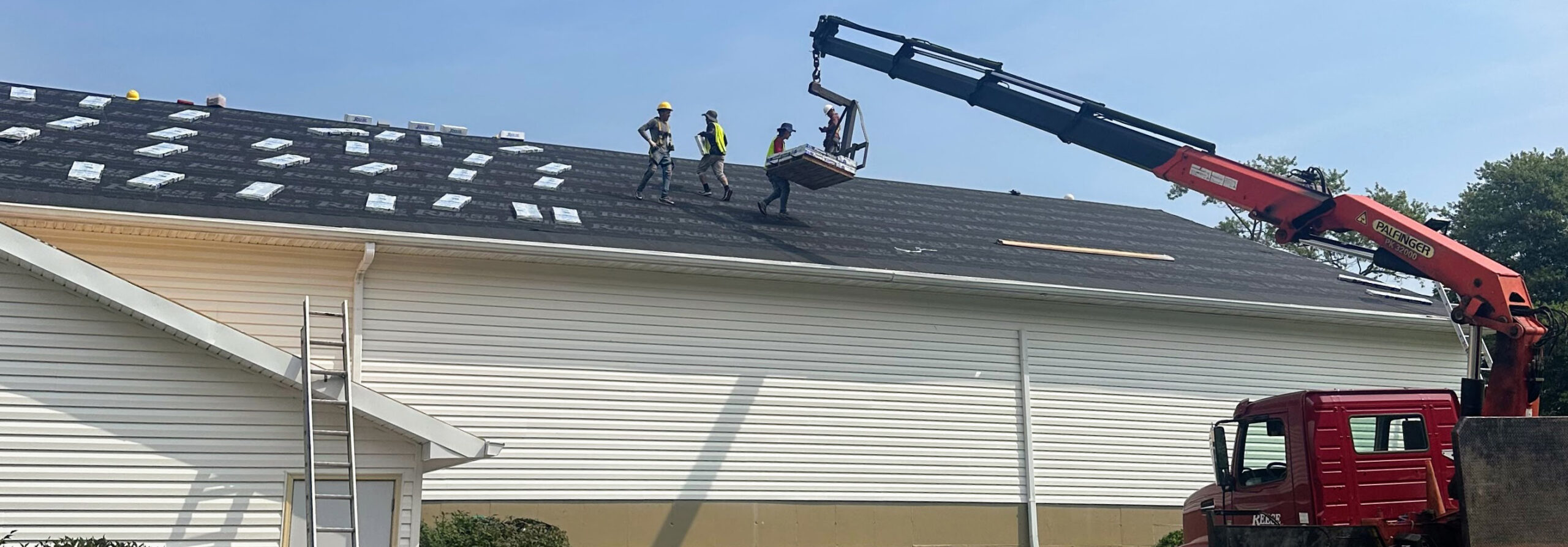 Roofing contractors working with a boom truck on a commercial roof replacement at a church in Bloomington, Indiana.