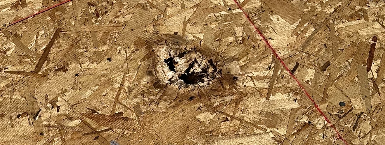 Close-up of a damaged roof with visible hole from hail impact, surrounded by fragmented wood chips.